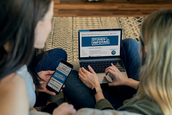 Zwei Mädchen sitzen auf dem Boden vor einem aufgeklappten Laptop auf dem Studienfotag zu lesen ist.
