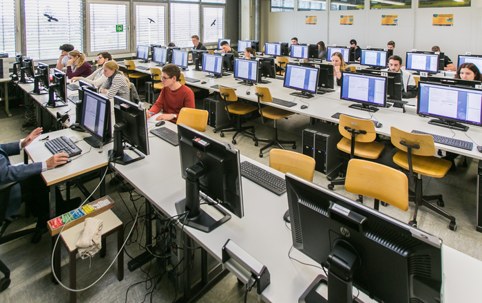 Ein Professor und Studierende sitzen in einem Hörsaal an Computern