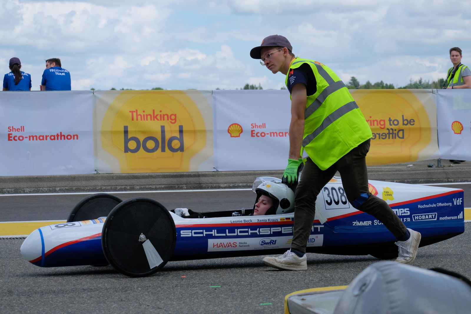 Der Schluckspecht S6, ein zigarrenförmiges blau-weißes Fahrzeug, wird mit einer Pilotin darin von einem Mann in Warnweste an den Start geschoben  