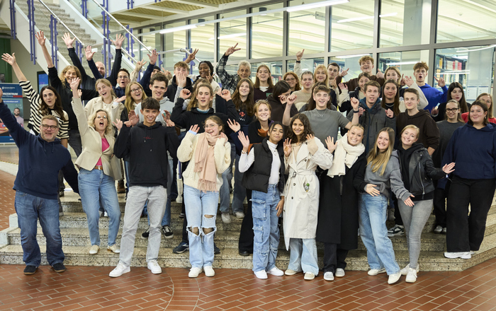 Gruppenfoto der Zwölftklasser und der Organisatoren mit jubelnd nach oben gerissenen Armen im Foyer von Bebäude B auf der Treppe vor der Bibliothek 