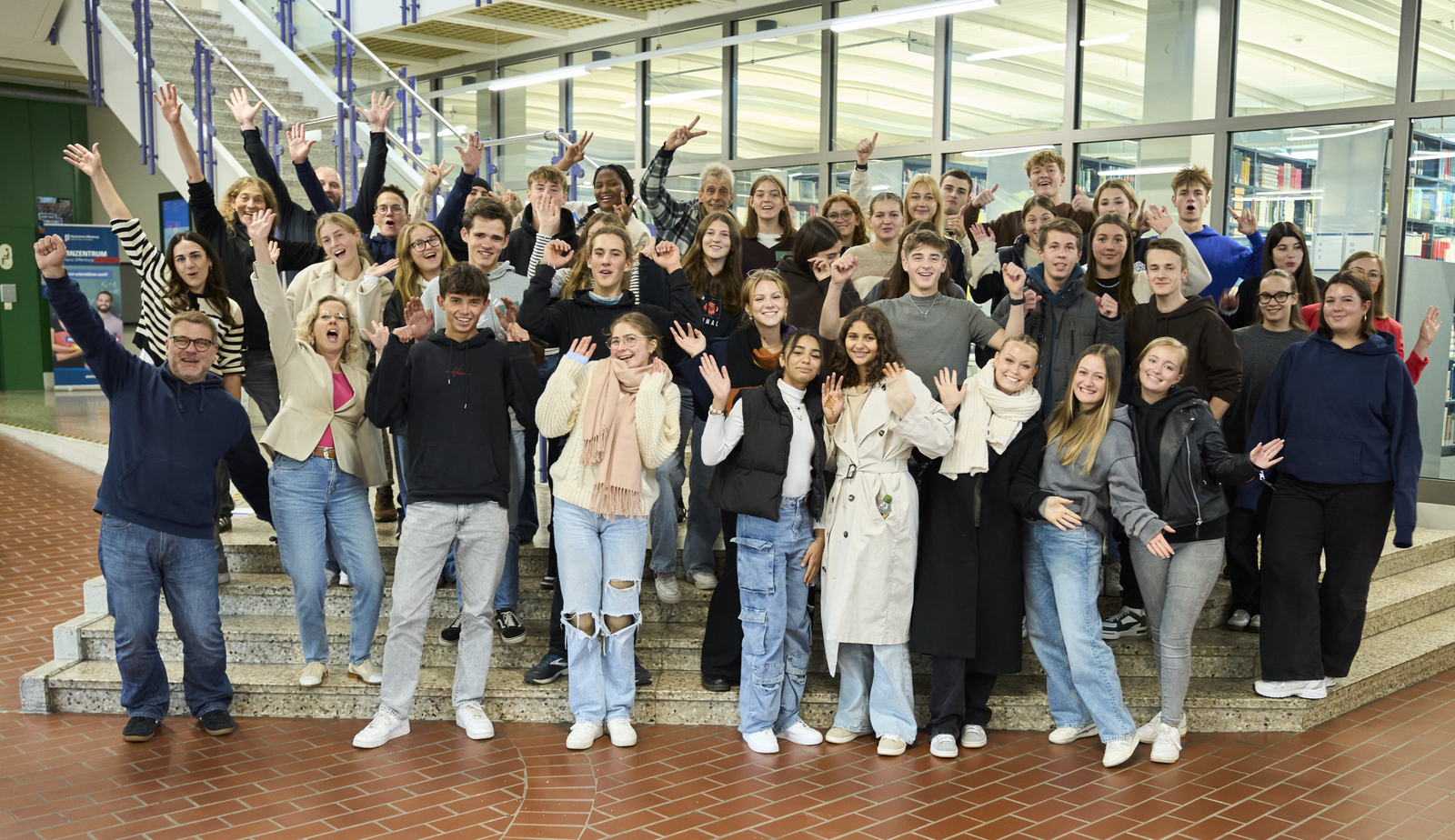 Gruppenfoto der Zwölftklasser und der Organisatoren mit jubelnd nach oben gerissenen Armen im Foyer von Bebäude B auf der Treppe vor der Bibliothek 