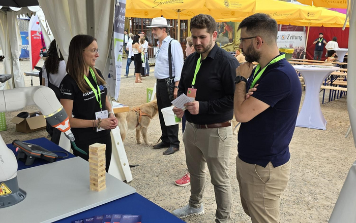 drei Personen, die sich neben einem Roboterarm unterhalten