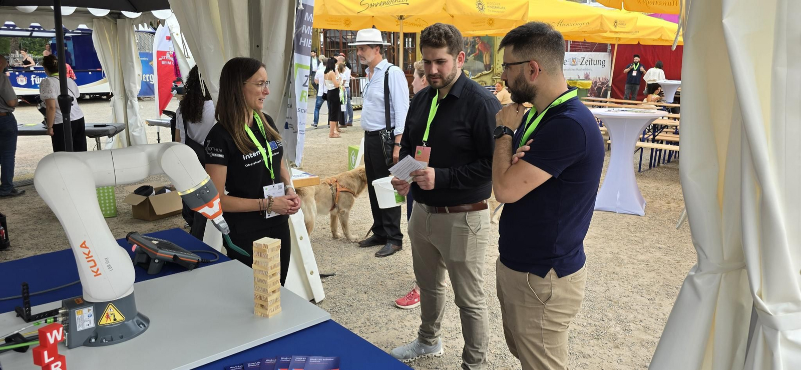 drei Personen, die sich neben einem Roboterarm unterhalten