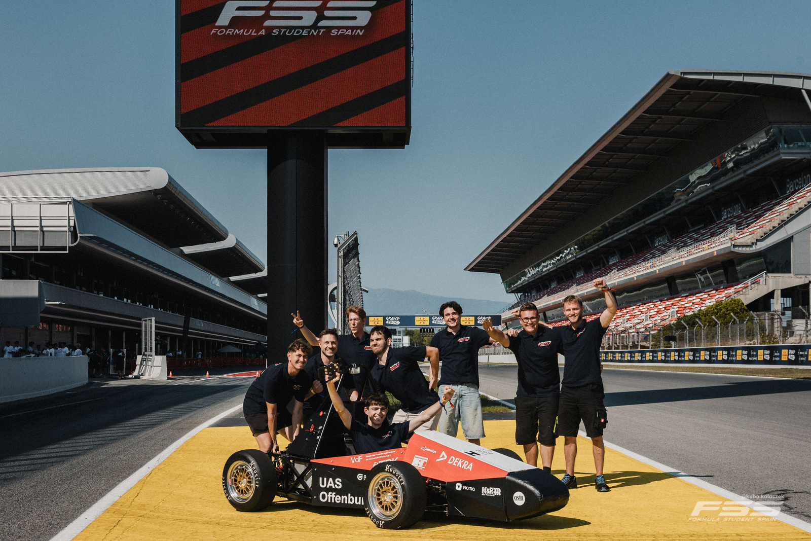 Das Team in lustigen Posen hinter dem Auto auf dem Circuit.