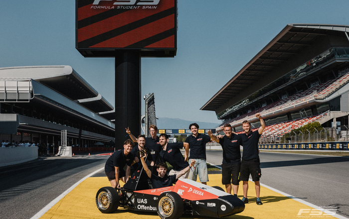 Das Team in lustigen Posen hinter dem Auto auf dem Circuit.