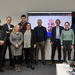 Gruppenbild der Projektbeteiligten vor einem Bildschirm auf dem ein online zugeschalteter Projektbeteiligter zu sehen ist
