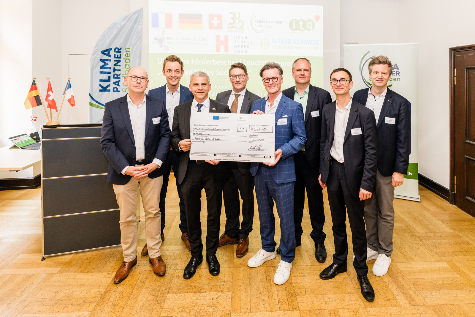 Gruppenfoto des Projektteams mit Staatssekretär Dr. Patrick Rapp und einem symbolischen Scheck