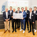 Gruppenfoto des Projektteams mit Staatssekretär Dr. Patrick Rapp und einem symbolischen Scheck
