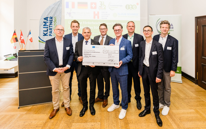 Gruppenfoto des Projektteams mit Staatssekretär Dr. Patrick Rapp und einem symbolischen Scheck