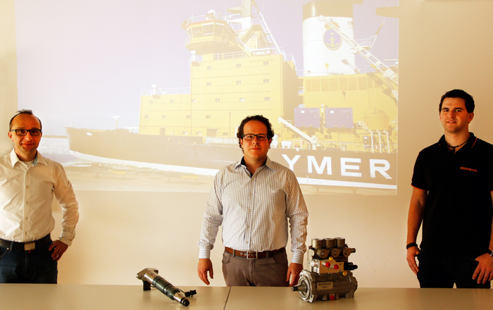Die HEINZMANN-Entwicklungsingenieure und ehemaligen Maschinenbau-Studenten der Hochschule Offenburg Simon Serrer (Mitte) und Andreas Ruf (rechts) mit ihrem früheren Professor Claus Fleig (links) vor einem per Beamer an die Wand geworfenen Bild eines Containerschiffs.
