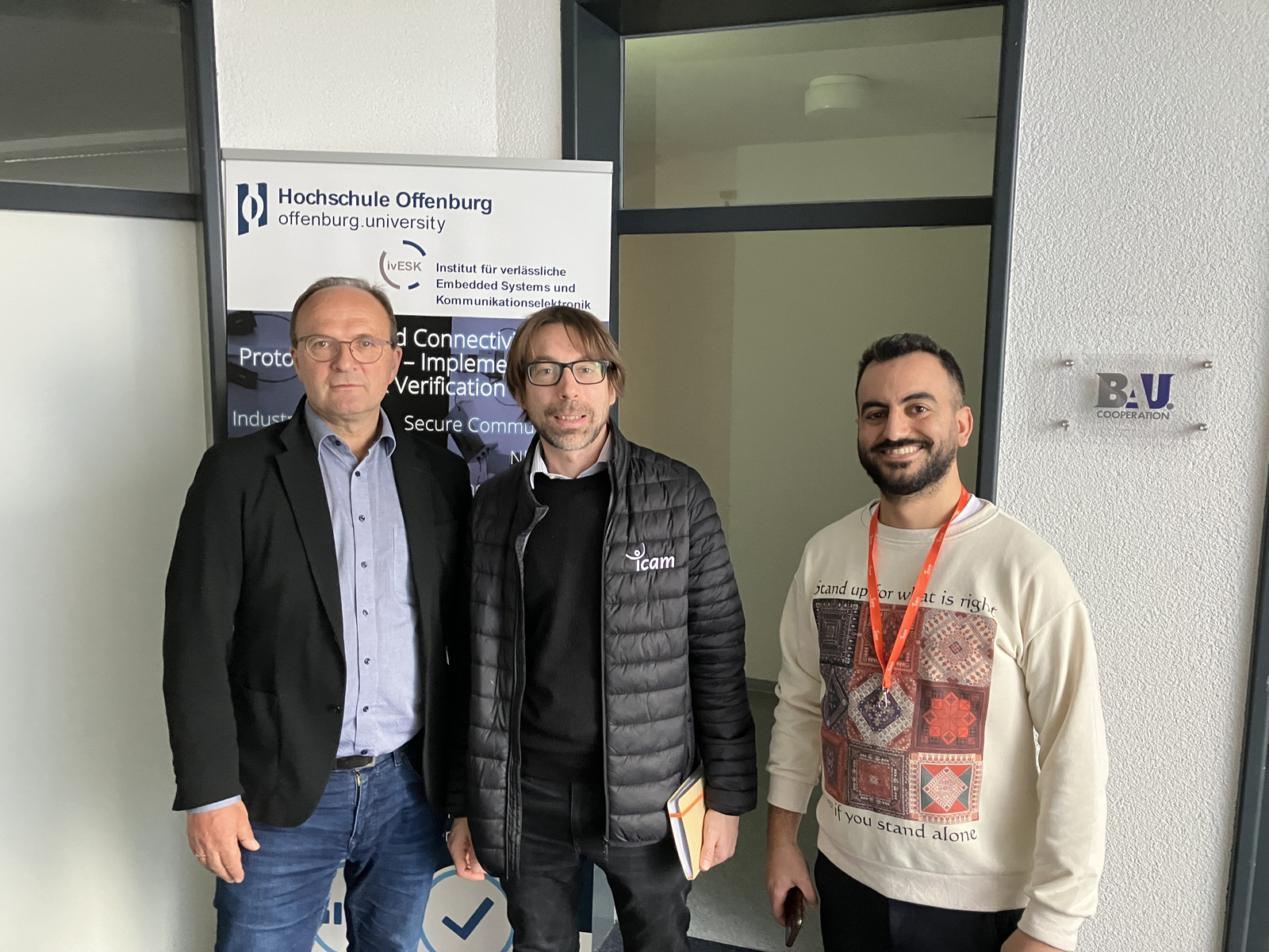 3 Personen nebeneinandervor dem RollUp des Institues