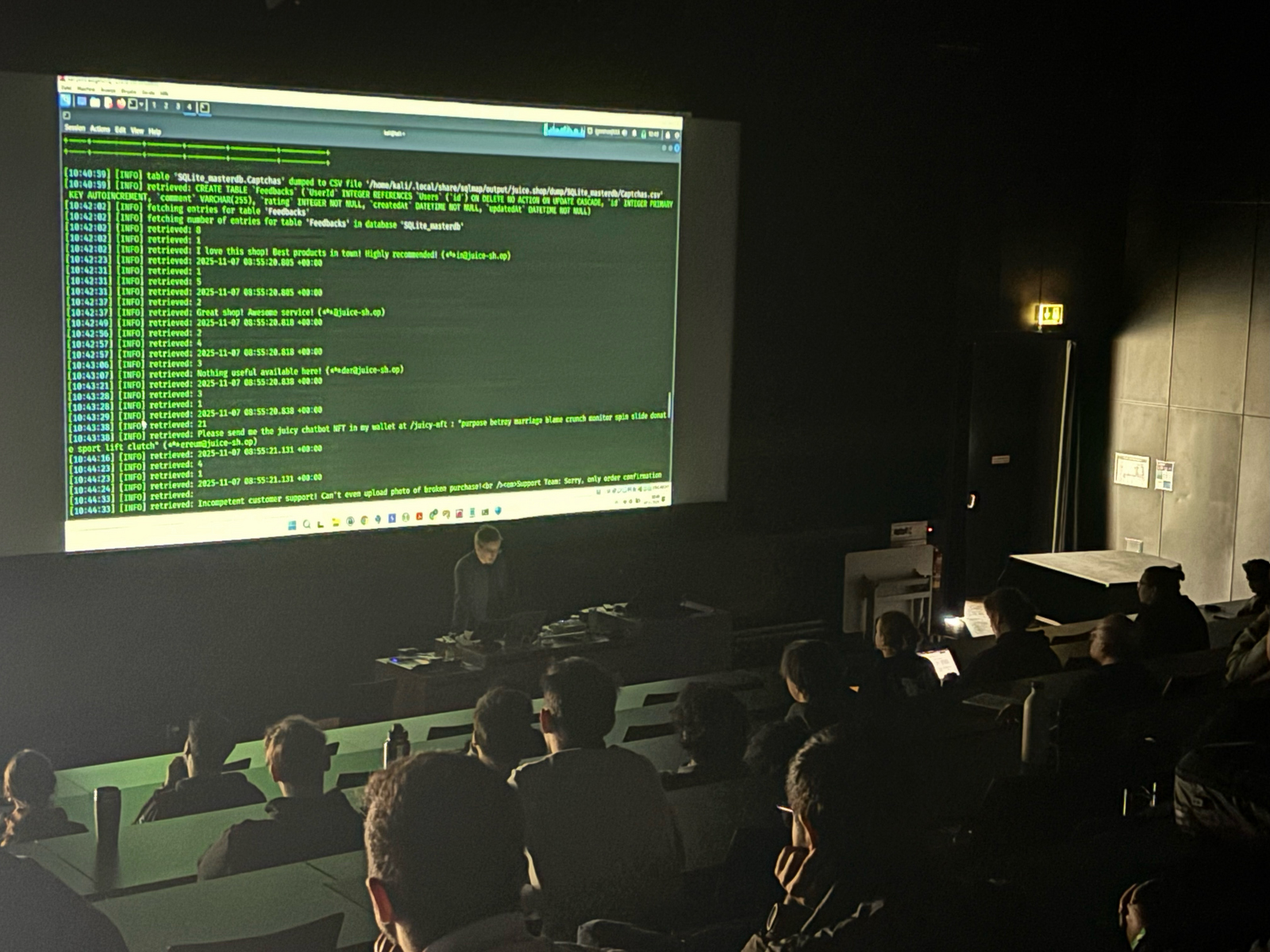 Ein Mann steht in einem dunklen Hörsaal am Rednerpult und auf der Leinwand hinter ihm sind Zahlenkolonnen zu sehen 