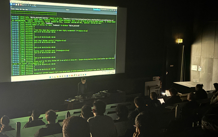 Ein Mann steht in einem dunklen Hörsaal am Rednerpult und auf der Leinwand hinter ihm sind Zahlenkolonnen zu sehen 