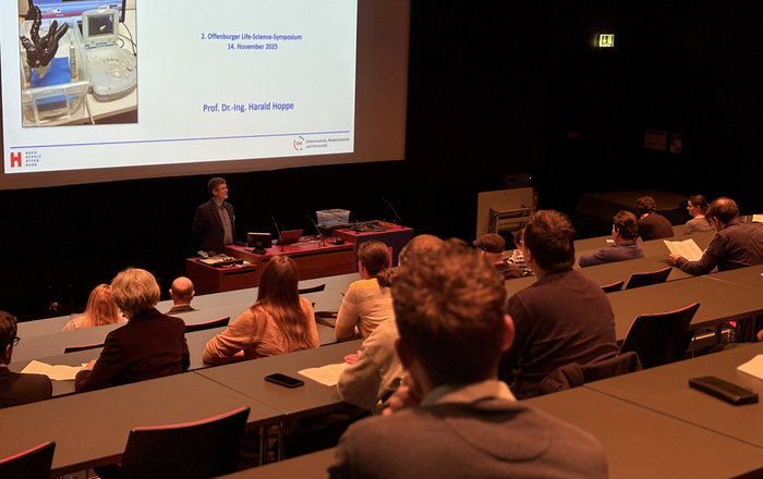 Ein Mann steht in einem Hörsaal vor einer Leinwand an einem Rednerpult.