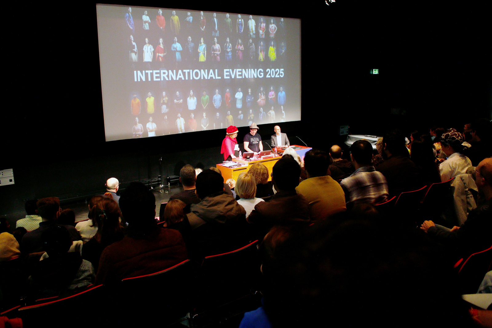 Drei Menschen stehen vor einer Leinwand an einem Rednerpult