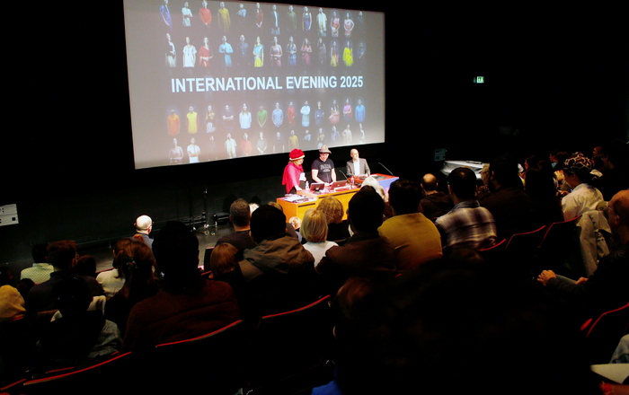 Drei Menschen stehen vor einer Leinwand an einem Rednerpult