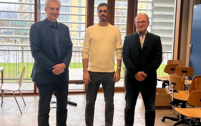 3 Personen stehend, Doktorand in der Mitte 