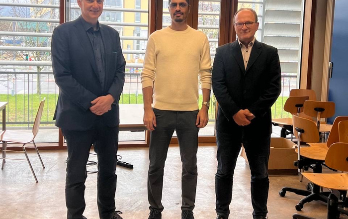 3 Personen stehend, Doktorand in der Mitte 