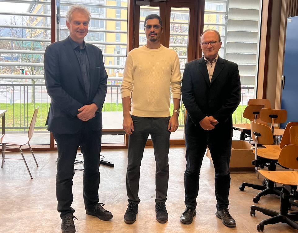 3 Personen stehend, Doktorand in der Mitte 