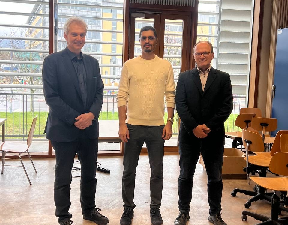 3 Personen stehend, Doktorand in der Mitte 