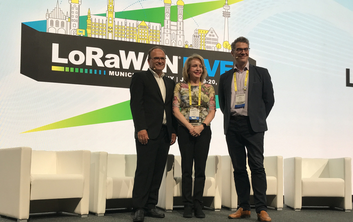 3 Personen stehen auf der der LoRWAN Live Bühne Veranstaltungs Logo im Hintergrund