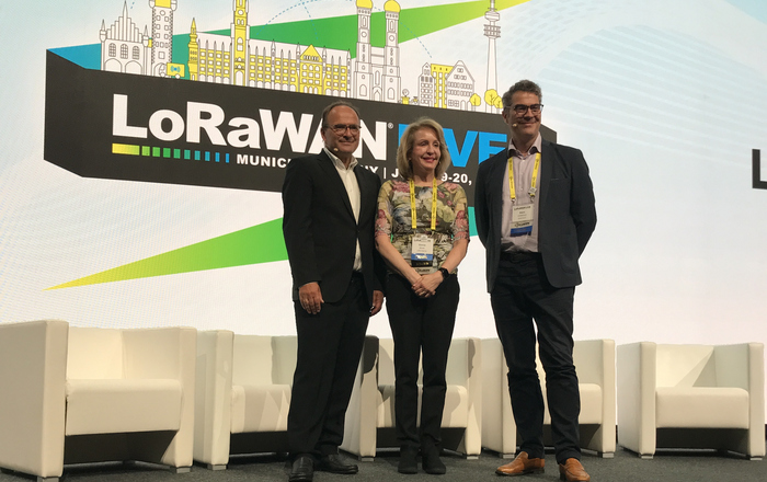3 Personen stehen auf der der LoRWAN Live Bühne Veranstaltungs Logo im Hintergrund