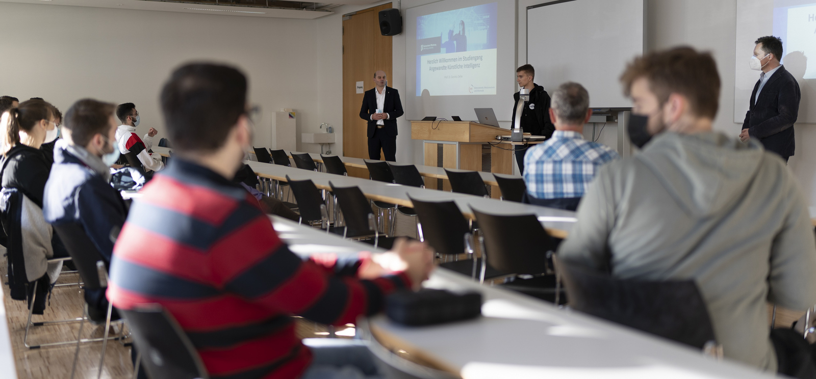 ektor Prof. Dr. Stephan Trahasch (links), Prorektor Prof. Dr. Oliver Schäfer (rechts) und der AStA-Vorsitzende Fabian Scheuch (Mitte) stehen bei der Begrüßung der Erstsemester im Studiengang Angewandte Künstliche Intelligenz vor den sitzenden neuen Studierenden.