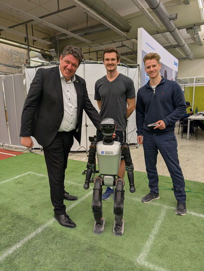 Drei Männer mit einem humanoiden Roboter auf einem Fußballfeld in einer Halle