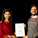 A woman in traditional Indian dress and a man in a woolen sweater hold a certificate