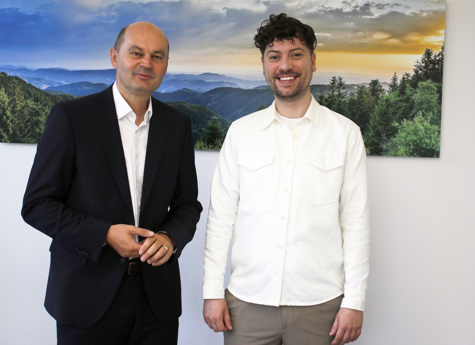 Zwei Männer stehen vor einem Schwarzwaldfoto und schauen in die Kameraa