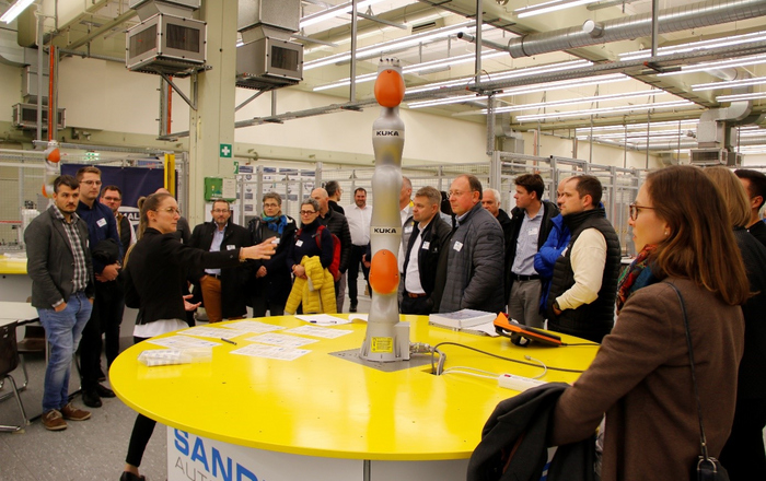 WLRI Mitarbeiterin zeigt den Besuchern des Labors den KUKA-Roboterarm