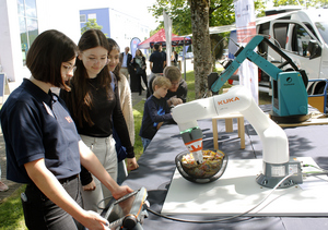 Junge Besucher*innen bedienen Greifarmroboter auf dem Campus
