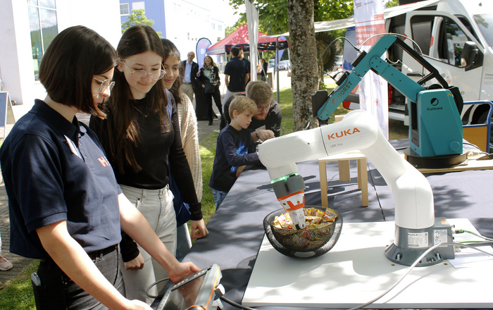 Junge Besucher*innen bedienen Greifarmroboter auf dem Campus