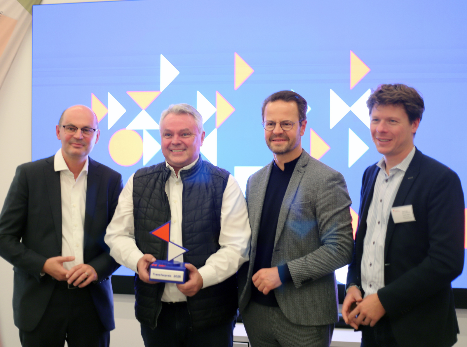 Vier Männer stehen in einer Reihe, der Zweite von links hält einen Award in Händen