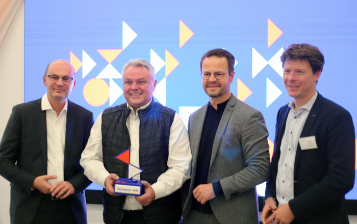 Vier Männer stehen in einer Reihe, der Zweite von links hält einen Award in Händen