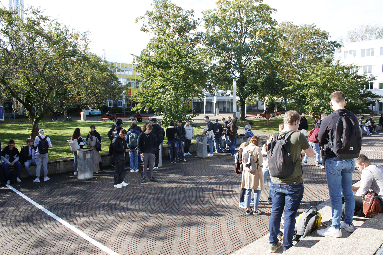 Studierenden stehen und sitzen auf dem Campus und trinken Kaffee