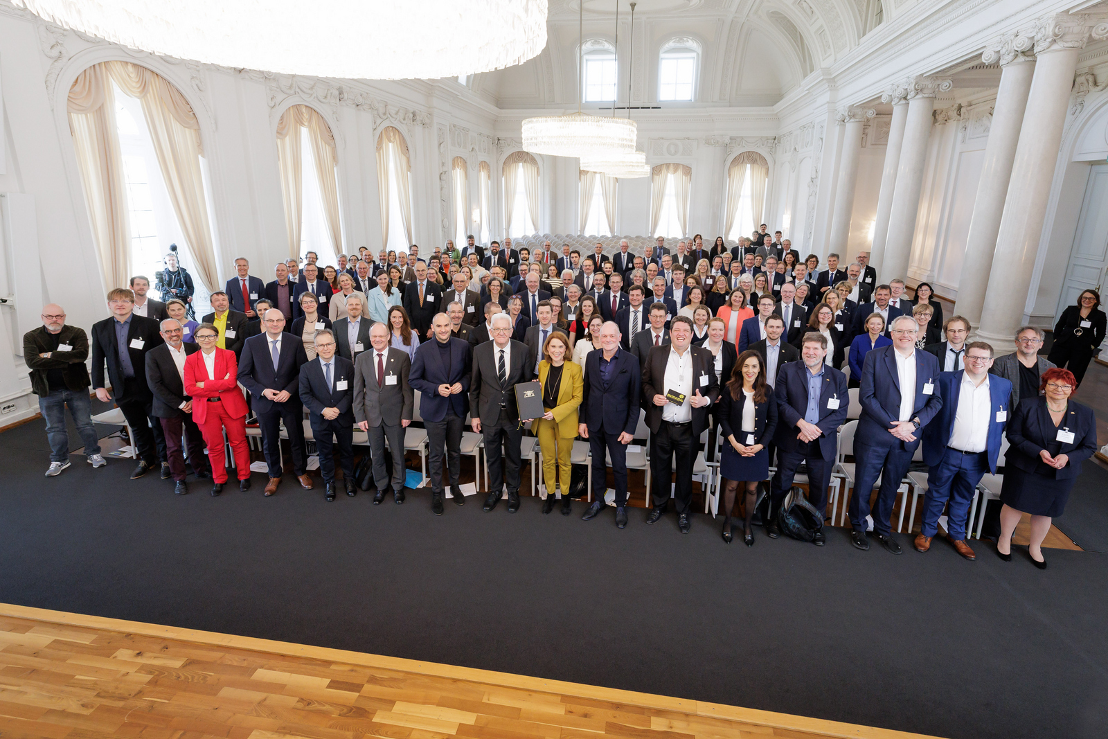 Gruppenfoto von stehenden Menschen im weißen Saal