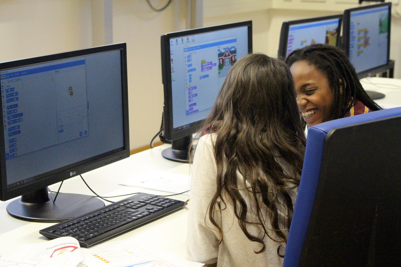 Zwei Mädchen sitzen vor einer Reihe von PC-Bildschirmen.