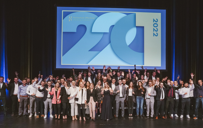 Gruppenfoto der jubelnden Absolvent*innen unter dem Logo der Abschlussfeier