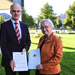 Ministerin Theresia Bauer (rechts) übergibt Prof. Dr. Volker Reuter (links), Vorsitzender der Rektorenkonferenz der HAW und des neu gegründeten Promotionsverbands, auf dem Rasen vor dem Ministerium die gerade unterzeichnete Rechtsverordnung zur Verleihung des Promotionsrechts. 