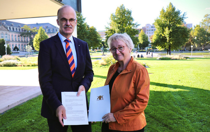 Ministerin Theresia Bauer (rechts) übergibt Prof. Dr. Volker Reuter (links), Vorsitzender der Rektorenkonferenz der HAW und des neu gegründeten Promotionsverbands, auf dem Rasen vor dem Ministerium die gerade unterzeichnete Rechtsverordnung zur Verleihung des Promotionsrechts. 