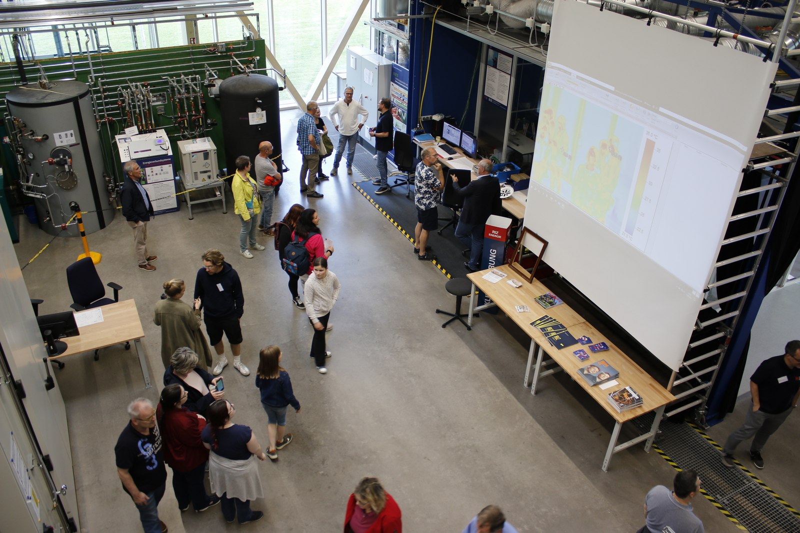 Menschen von oben vor einer Heizungsanlage und einer Leinwand mit Wärmedaten.