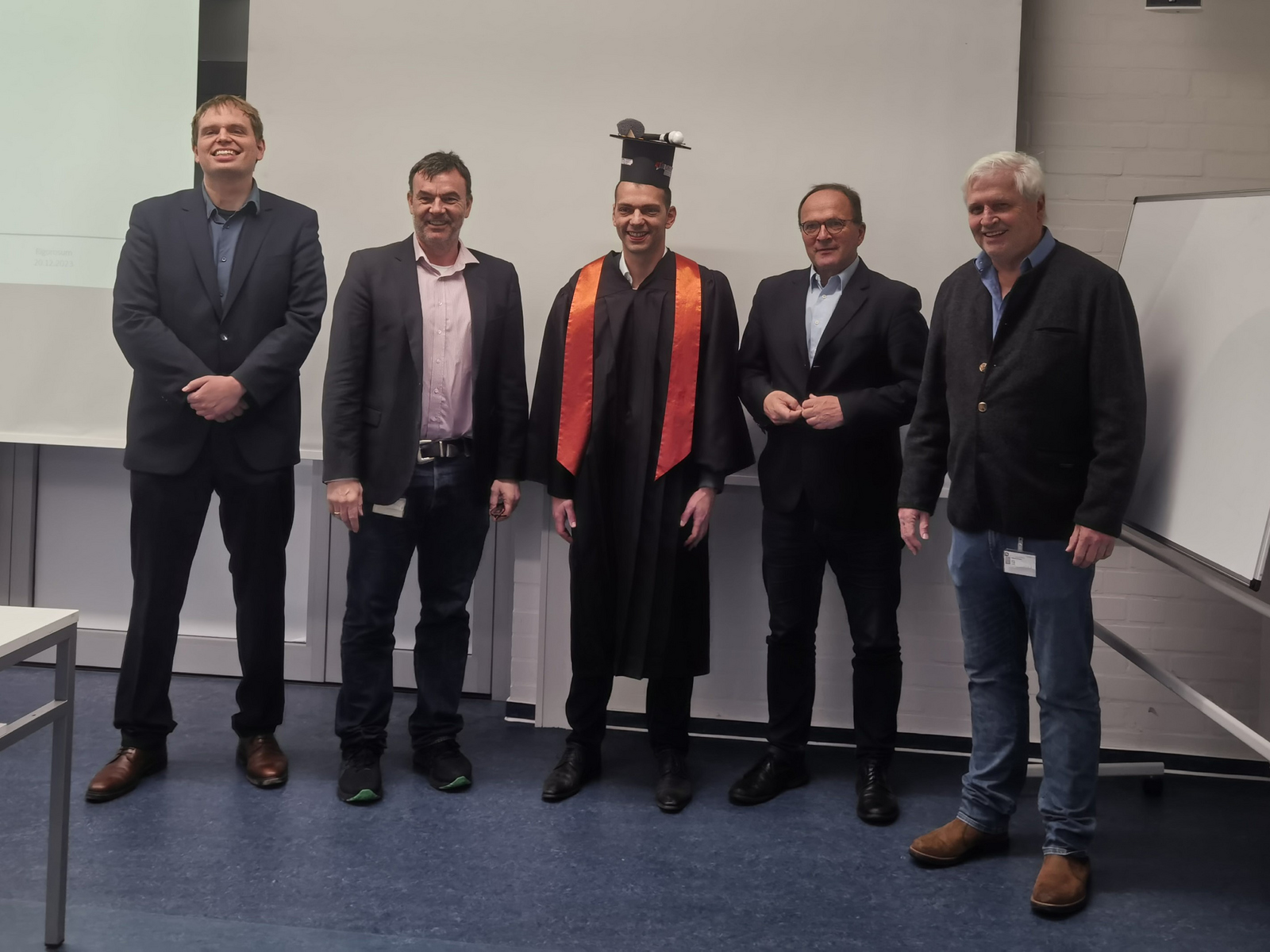 5 Personen in Reihe, die Mittlere Person tägt einen Doktorhut.