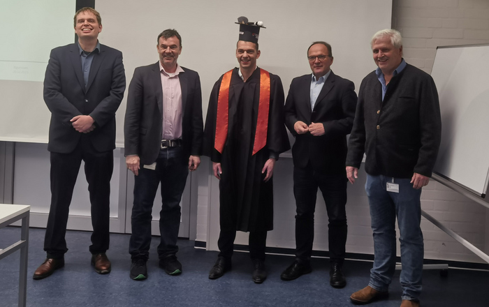 5 Personen in Reihe, die Mittlere Person tägt einen Doktorhut.