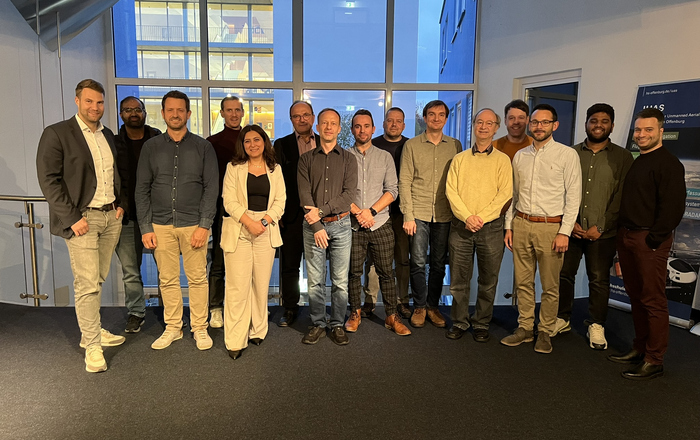 15 Personen stehen als Gruppe nebeneinander ein einer Reihe