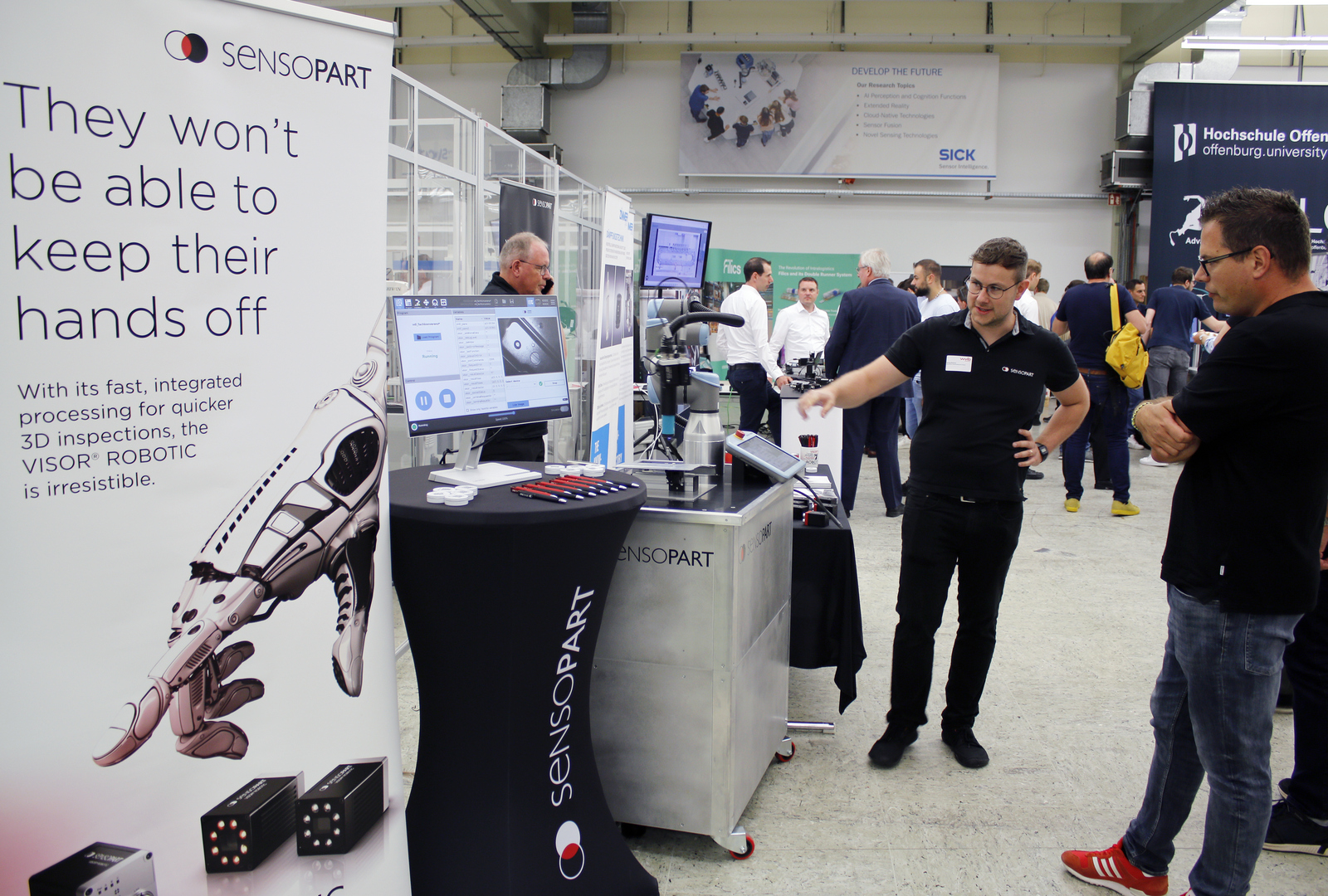 Zwei Männer stehen an einem Messestand, einer erklärt etwas