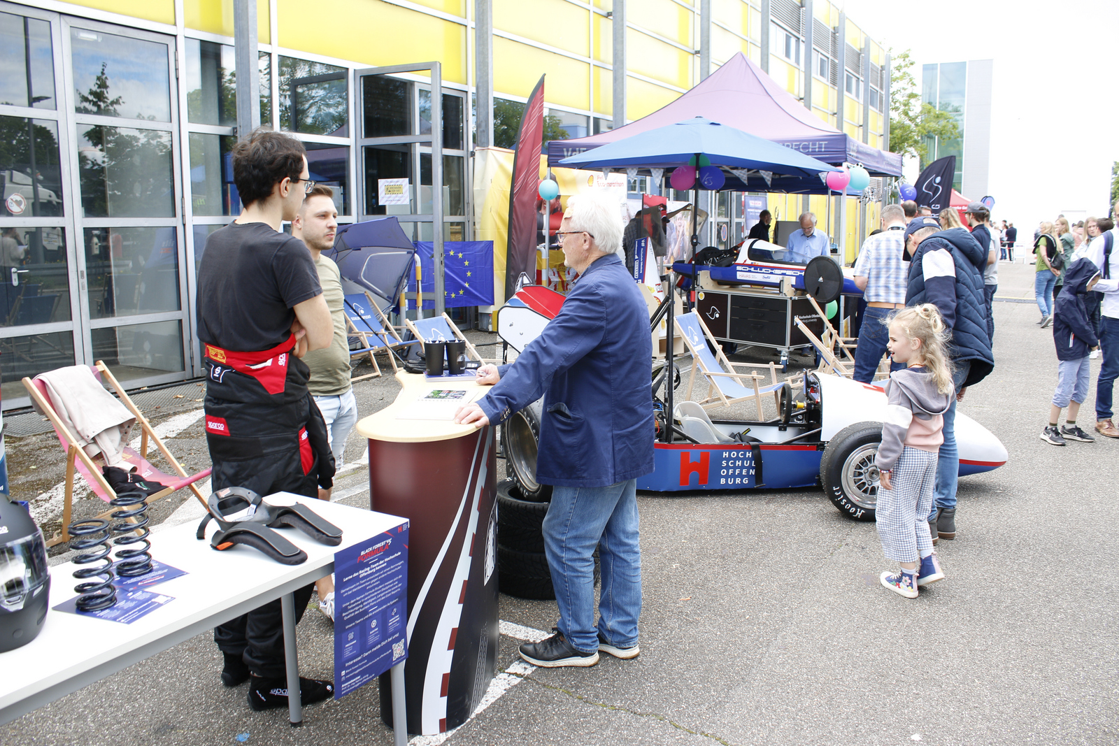Menschen betrachten die vor einem Gebäude aufgereihten Fahrzeuge 