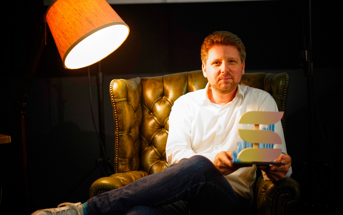 Moderator Kai Wissmann sitzt im Sessel und präsentiert die Shorts-Trophäe.