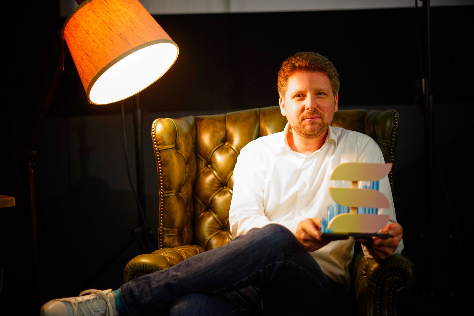 Moderator Kai Wissmann sitzt im Sessel und präsentiert die Shorts-Trophäe.