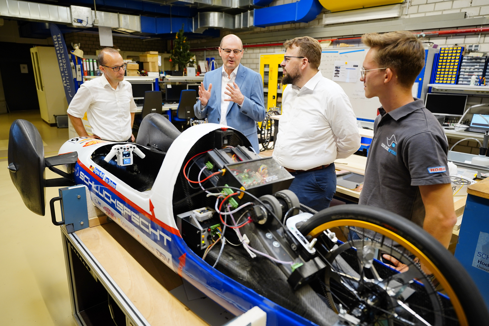 Claus Fleig, Stephan Trahasch, Martin Gassner-Herz und ein Student stehen hinter einem Fahrzeug ohne Motohaube und reden.
